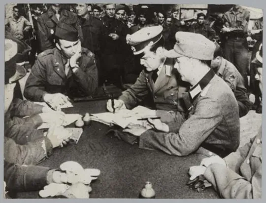 Les représentants allemands (major Engelken et lieutenant Bernstein) face au colonel Keating signent la reddition de la poche de Saint-Nazaire sur une table dressée à la hâte à Cordemais le 8 mai 1945, United States Army Signal Corps